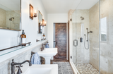 Pebble tile shower floor in primary bathroom with standing shower and dual pedestal sinks