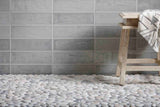 Round pebble mosaic tile flooring in a spa-style bathroom, paired with gray handmade-look subway wall tile and a carved wooden stool with a woven throw