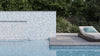 Poolside view with a stunning mosaic tile wall, featuring a waterfall and a lounge chair adorned with a turquoise pillow. Lush greenery completes the tranquil setting.